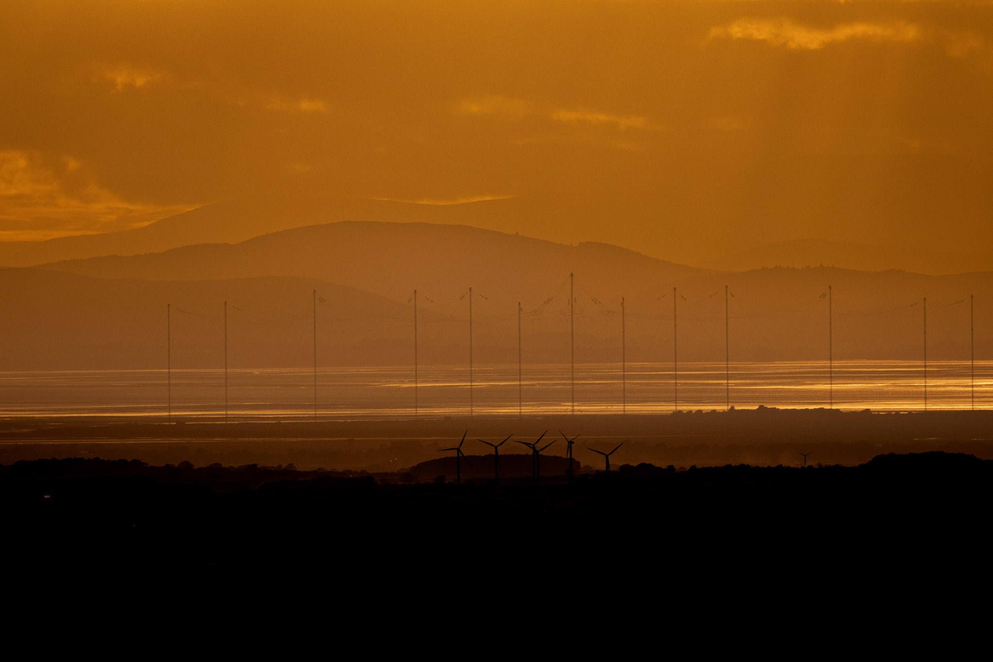 Wind turbines silhouetted beneath an amber sky